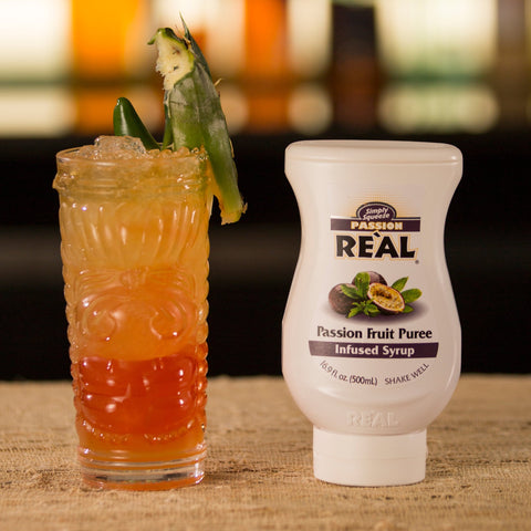 Bottle of Real passion fruit next to a cocktail in a bar setting. 