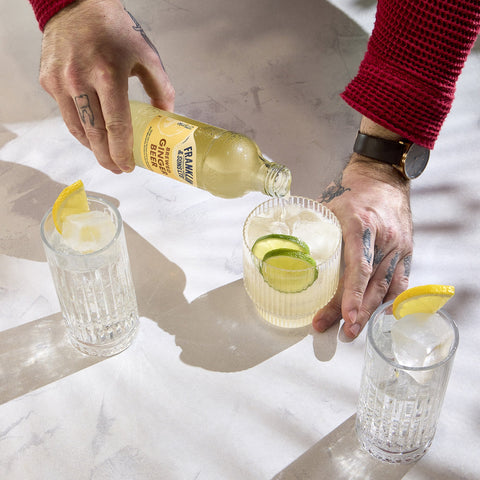 Someone pouring a bottle of Franklin & Sons brewed ginger beer into a glass with other glasses of brewed ginger beer on the table as well. 