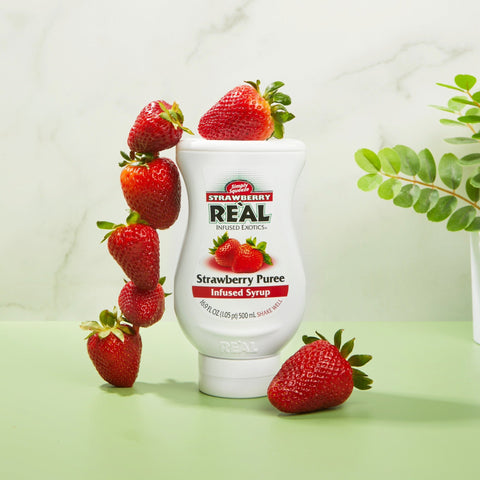 Bottle of Strawberry Reàl Strawberry Puree syrup with strawberries on a light green background