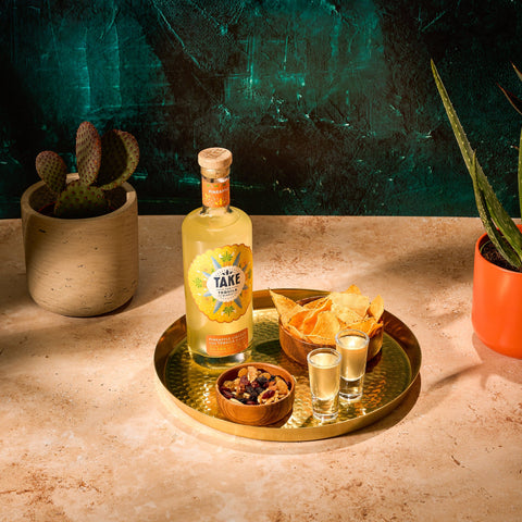 Bottle of Take Tequila on a tray with chips and shots against a textured green wall.