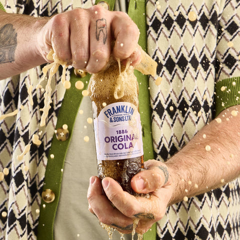 Someone opening a bottle of Franklin & Sons 1886 original cola as it splashes. 