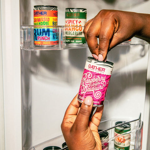 A person opening a can of GATHER raspberry ripple daiquiri with other cans of GATHER in the fridge in the background. 