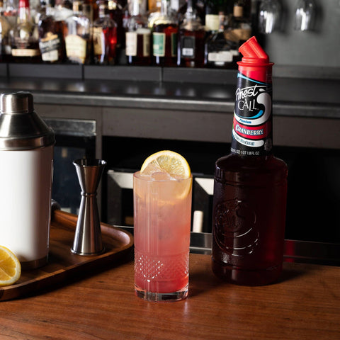 A cranberry cocktail made with Finest Call Premium Cranberry juice mix, with the Finest Call bottle placed behind the cocktail. 