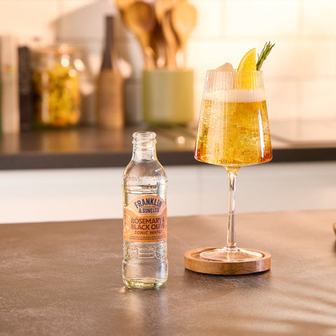A bottle of Franklin & Sons rosemary & black olive tonic water next to a glass where the tonic water has been used as a premium mixer. 