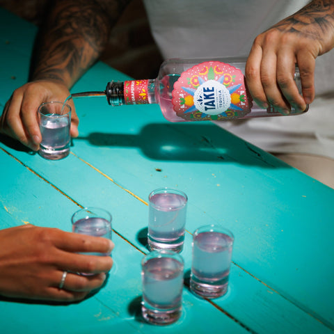 Person pouring Take tequila into shot glasses on a teal table. 