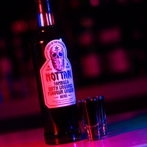 An alcoholic shot of Nottari Nero Sambuca  with the Nottari bottle next to the shot. 