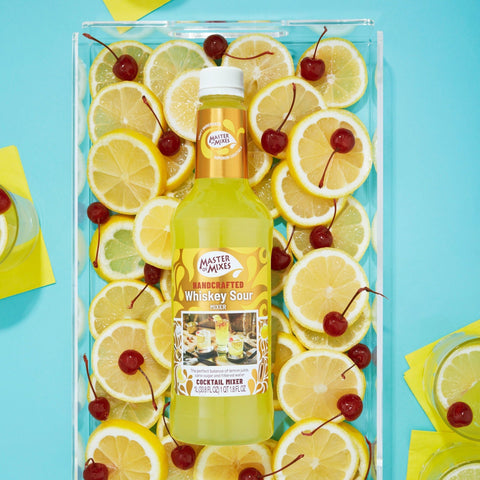 Bottle of Master of Mixes whiskey sour surrounded by lemon slices and cherries on a blue background.