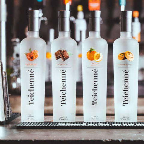 Four bottles of Teichenne schnapps in flavours strawberry, chocolate, peach & butterscotch lined up on a bar. 