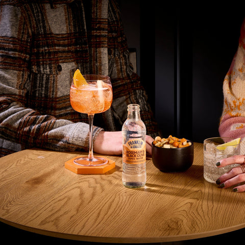 Two people sitting at a able drinking, where the drinks have been made using Franklin & Sons rosemary and black olive tonic water as a premium mixer. 
