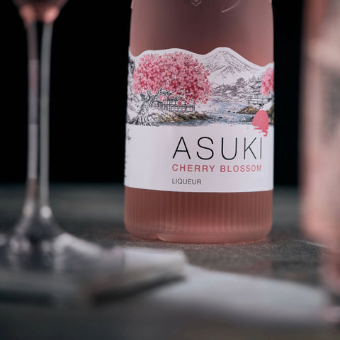 Bottle of Asuki Cherry Blossom Liqueur with a cherry blossom label on a dark surface.