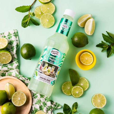 Bottle of Master of Mixes Mojito mix surrounded by limes, lemons, and mint leaves on a light green background.