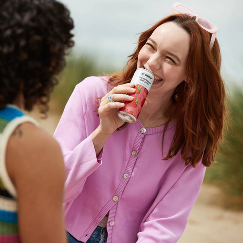 A woman talking to her friend drinking an All Shook Up Strawberry Daiquiri canned cocktail. 