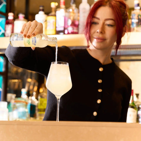 Person pouring a Franklin & Sons into a glass at a bar.